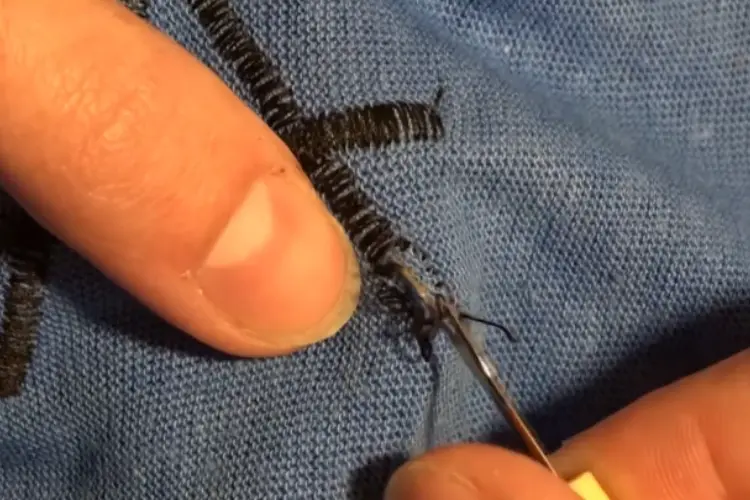 Close-up of tweezers gently plucking residual threads from the fabric of a shirt.