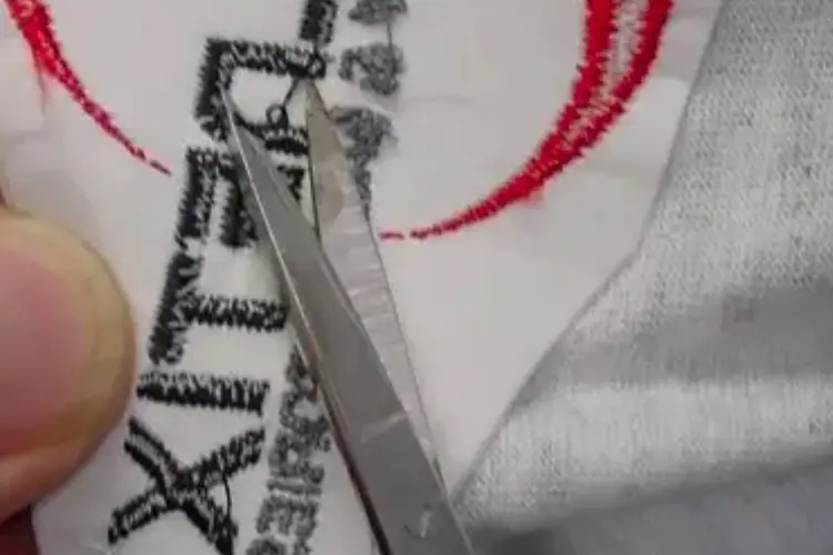 Close-up of hands using small scissors to carefully cut threads of embroidery on a shirt.