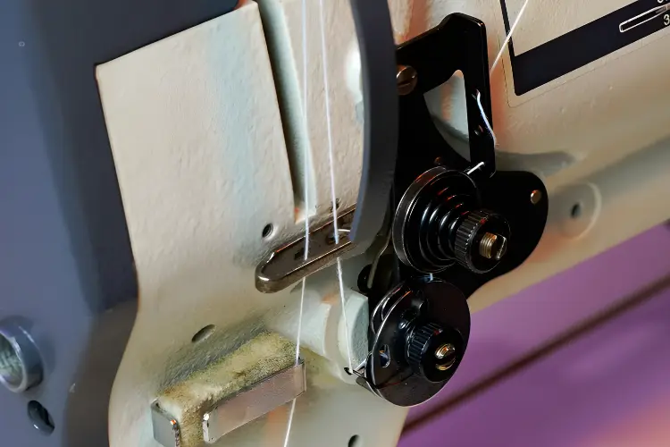 A close-up of a sewing machine's tension dial and tension discs.